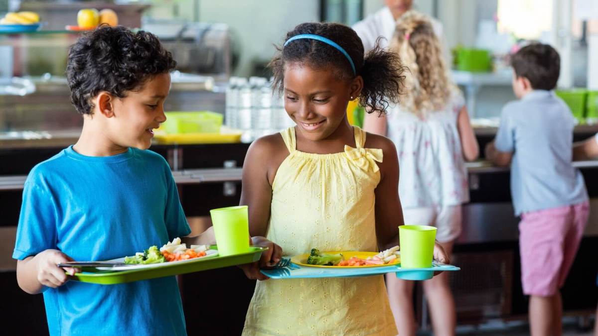 Children at school carrying trays of healthy food and smiling