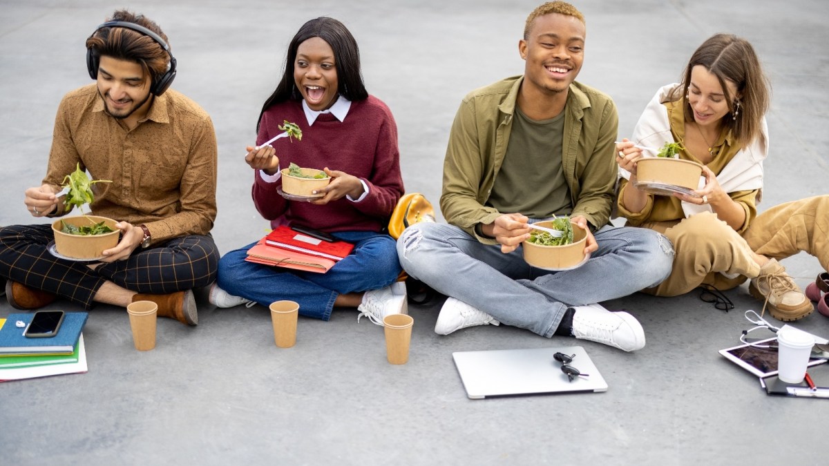 Students sit on the ground eating salad with their text books