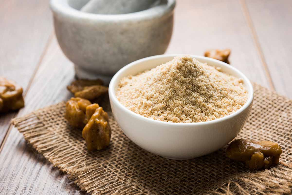 A close up horizontal image of a bowl of powdered asafetida spice set on a wicker mat on a wooden surface.